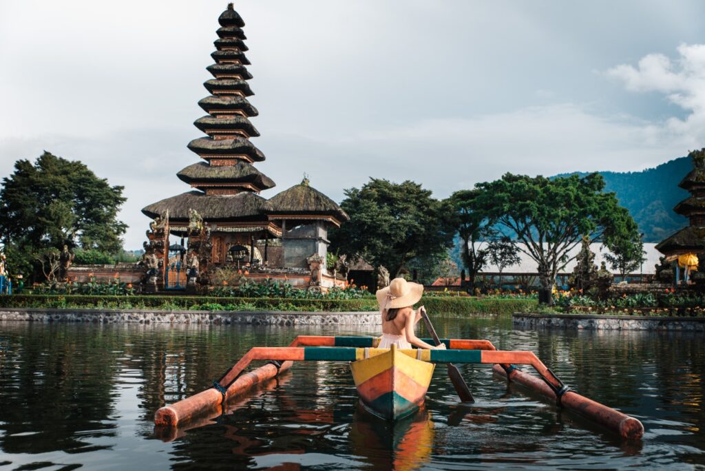 Young woman traveler paddling on a wooden boat at Pura Ulun Danu
